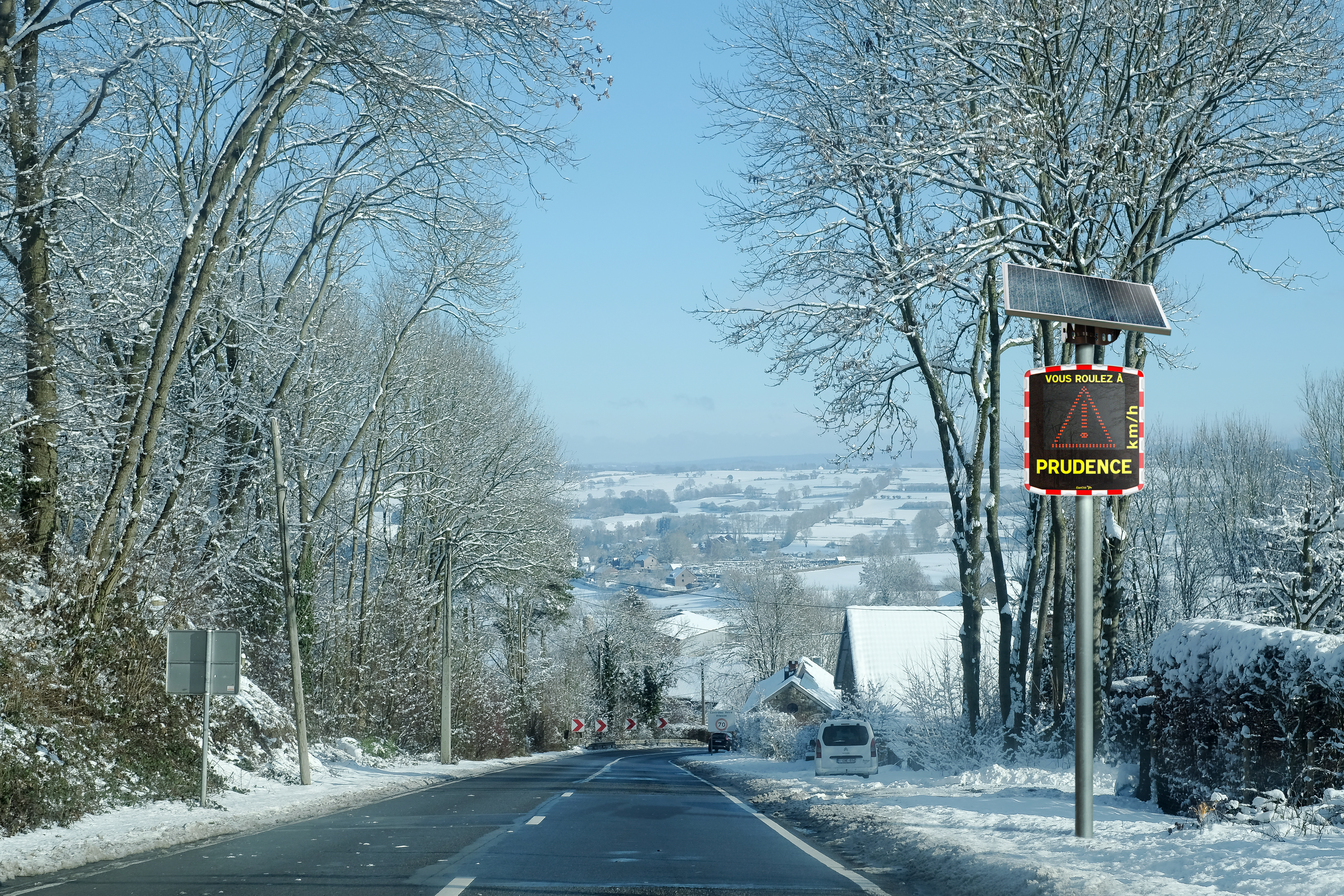 Un radar pédagogique mobile installé aux abords d'une route communale enneigée et qui affiche un triangle danger.