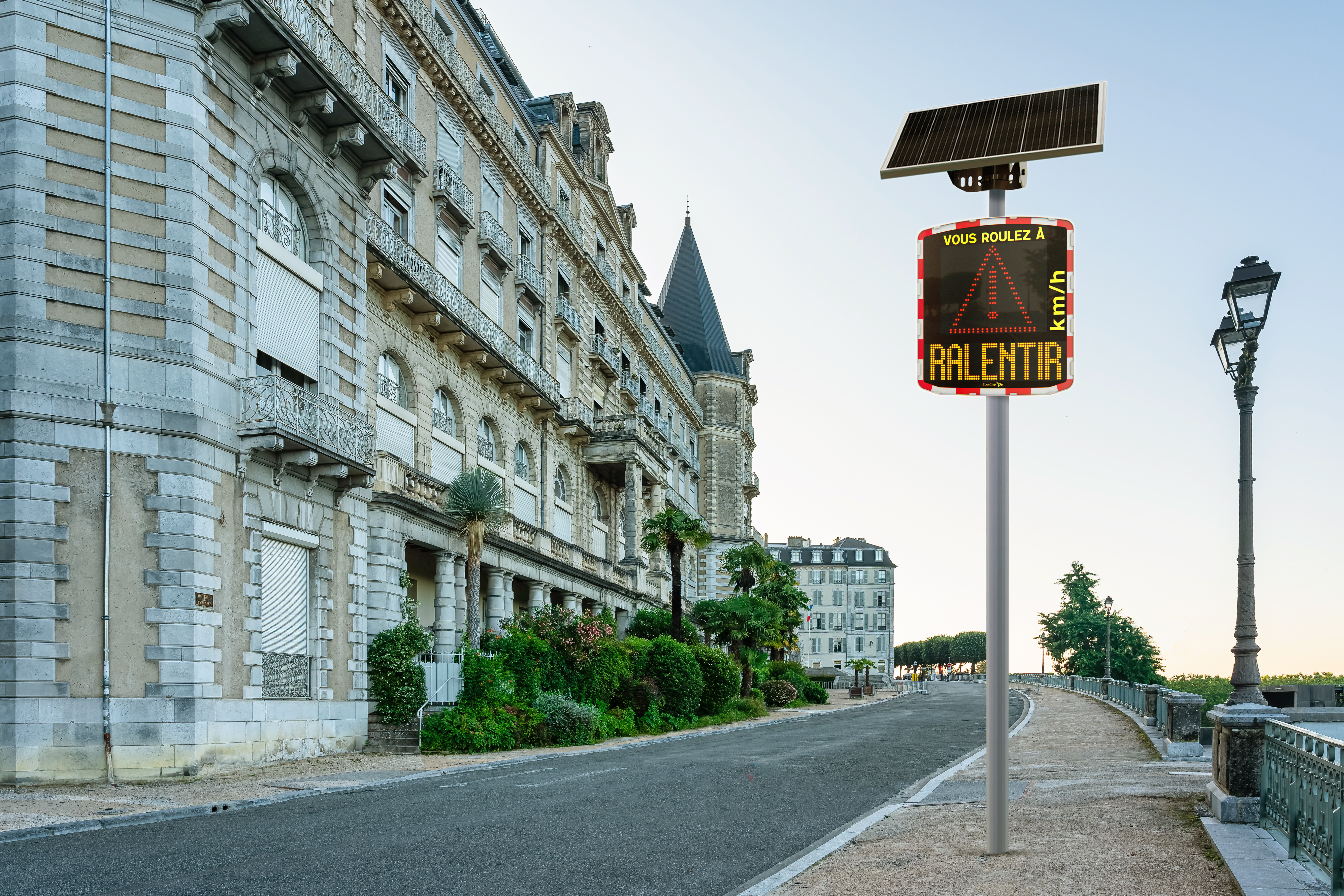 Un radar pédagogique solaire instalé aux abords d'une rue piétonne qui affiche un triangle et un message de prévention "RALENTIR"
